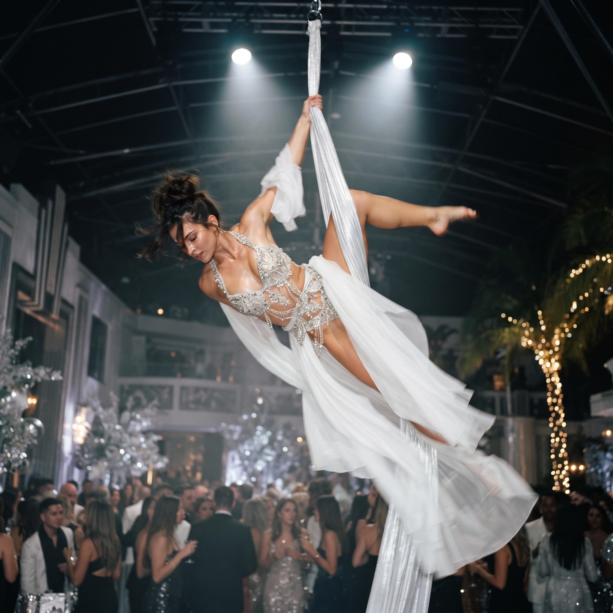 Aerial silk performer in a flowing white gown above a crowded nightlife event floor